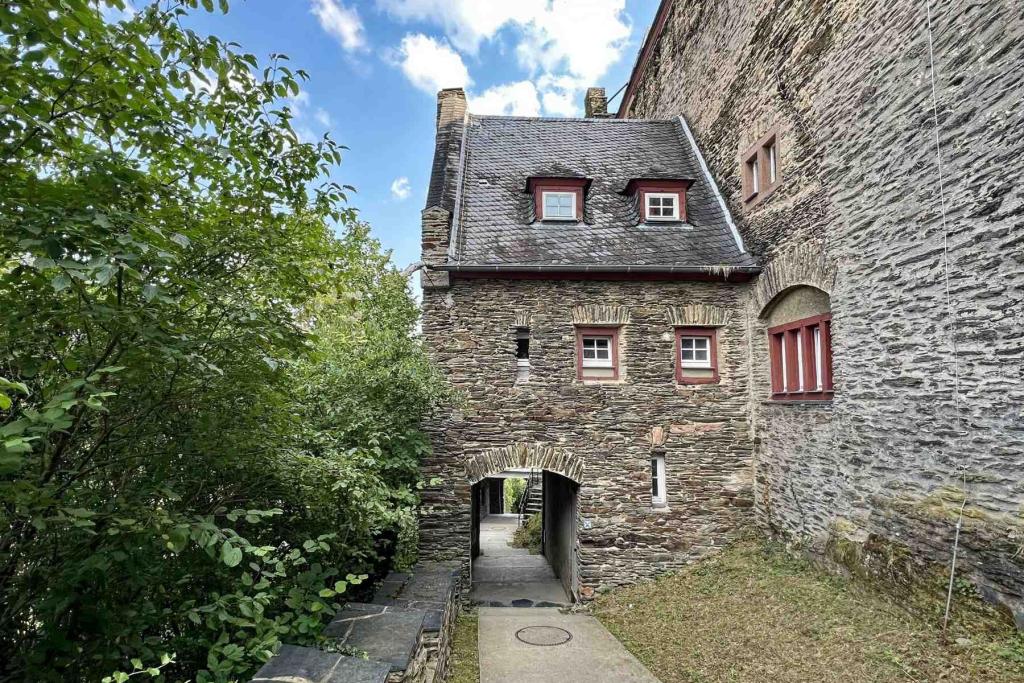 Ein historisches Gebäude mit grauem Stein und einem angrenzenden grünen Innenhof, umgeben von Bäumen und Mauern.